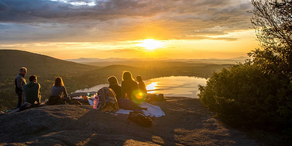 people sitting on hill watching sunset